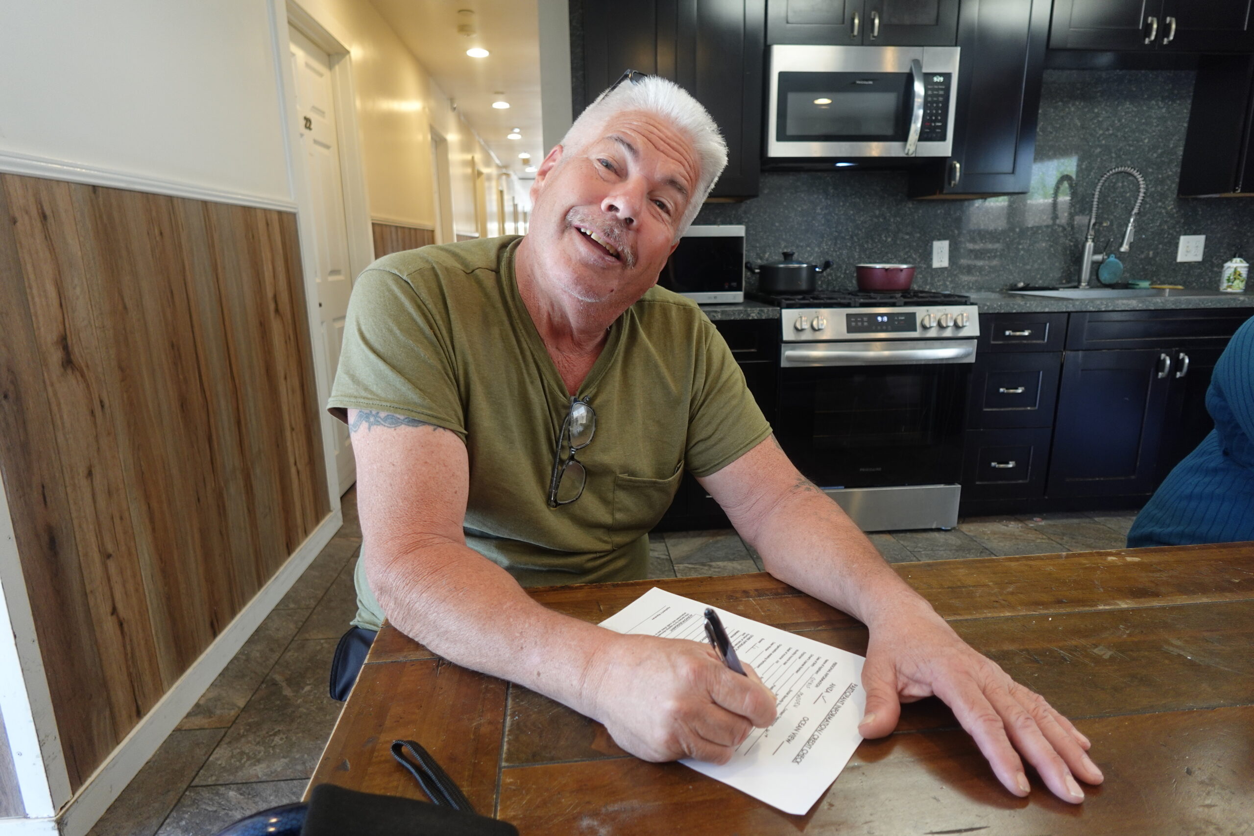 Chris smiling and posing at the camera while writing something on a piece of paper